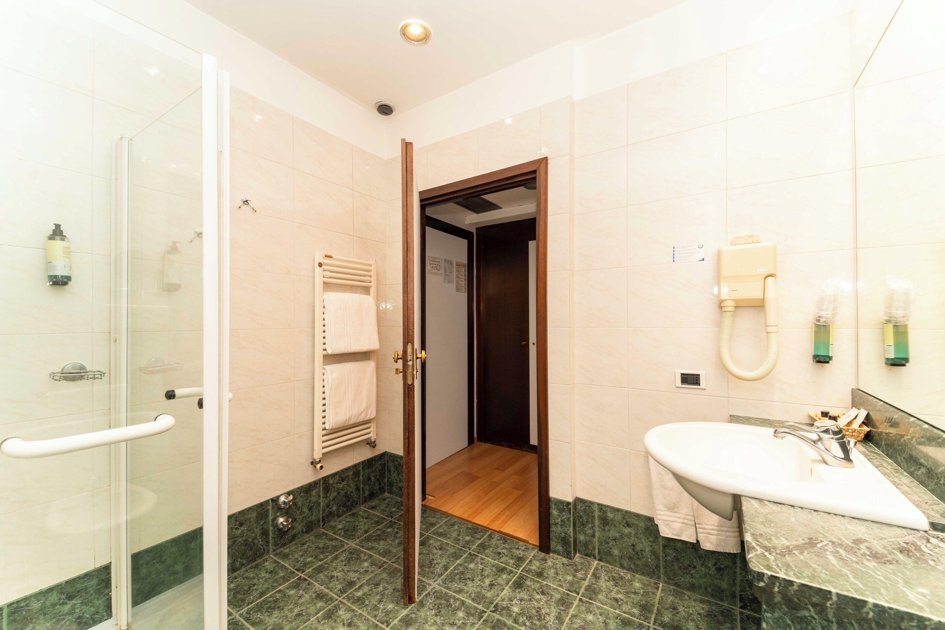 Une salle de bain dotée d’une douche à parois de verre, d’un lavabo avec un plan de toilette en marbre et d’une porte en bois donnant sur une autre pièce.