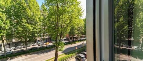 Vista desde una ventana sobre una calle bordeada de árboles y coches aparcados.