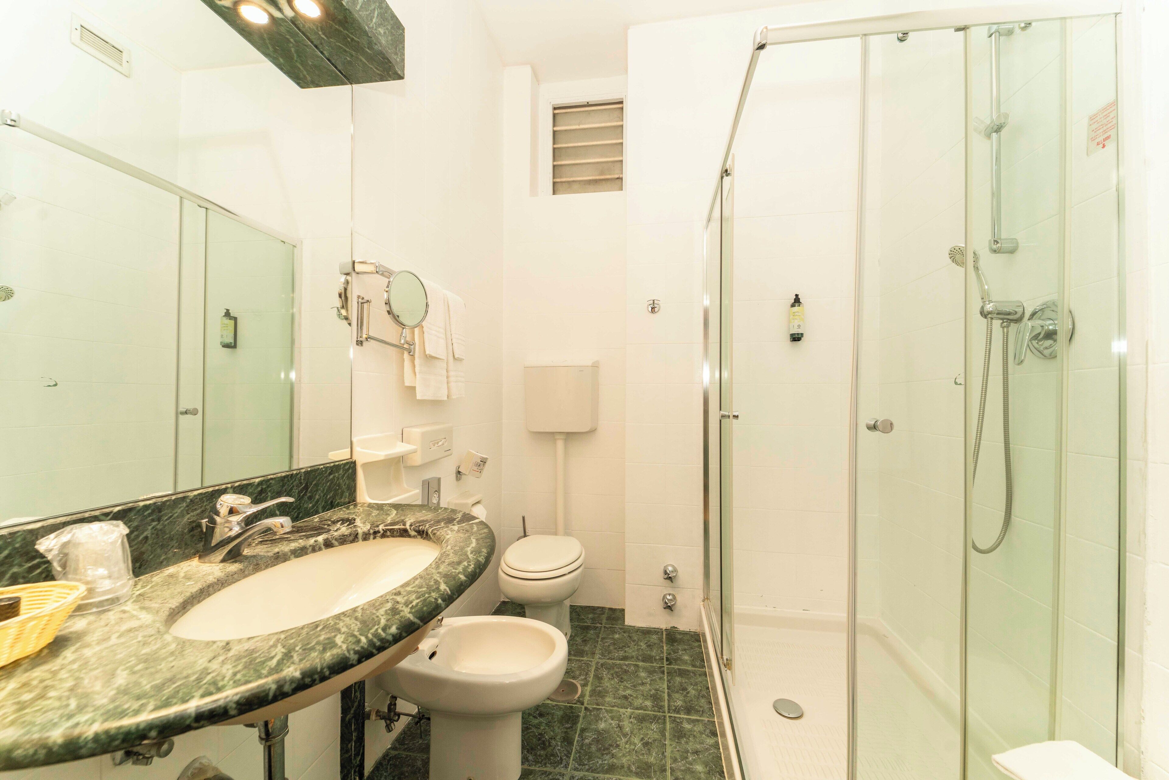 A bathroom with a marble sink, toilet, and glass-enclosed shower.