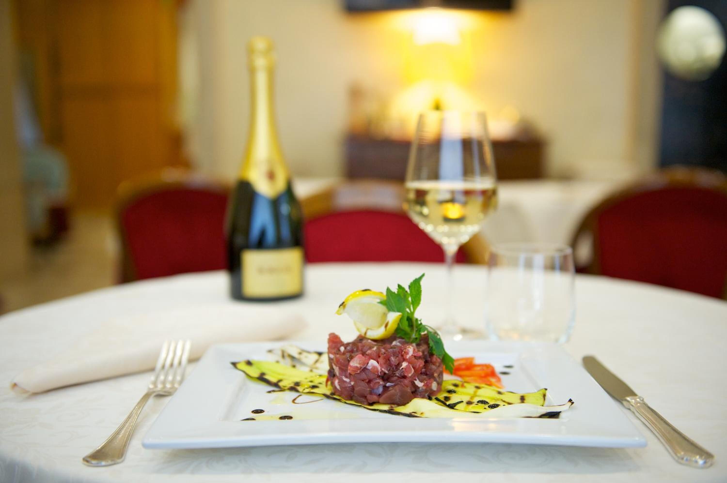 Una mesa de comedor con un plato de comida, una botella de vino y una copa de vino.