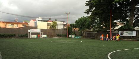 Un campo de fútbol con porterías, un anuncio en la banda lateral y un edificio al fondo.