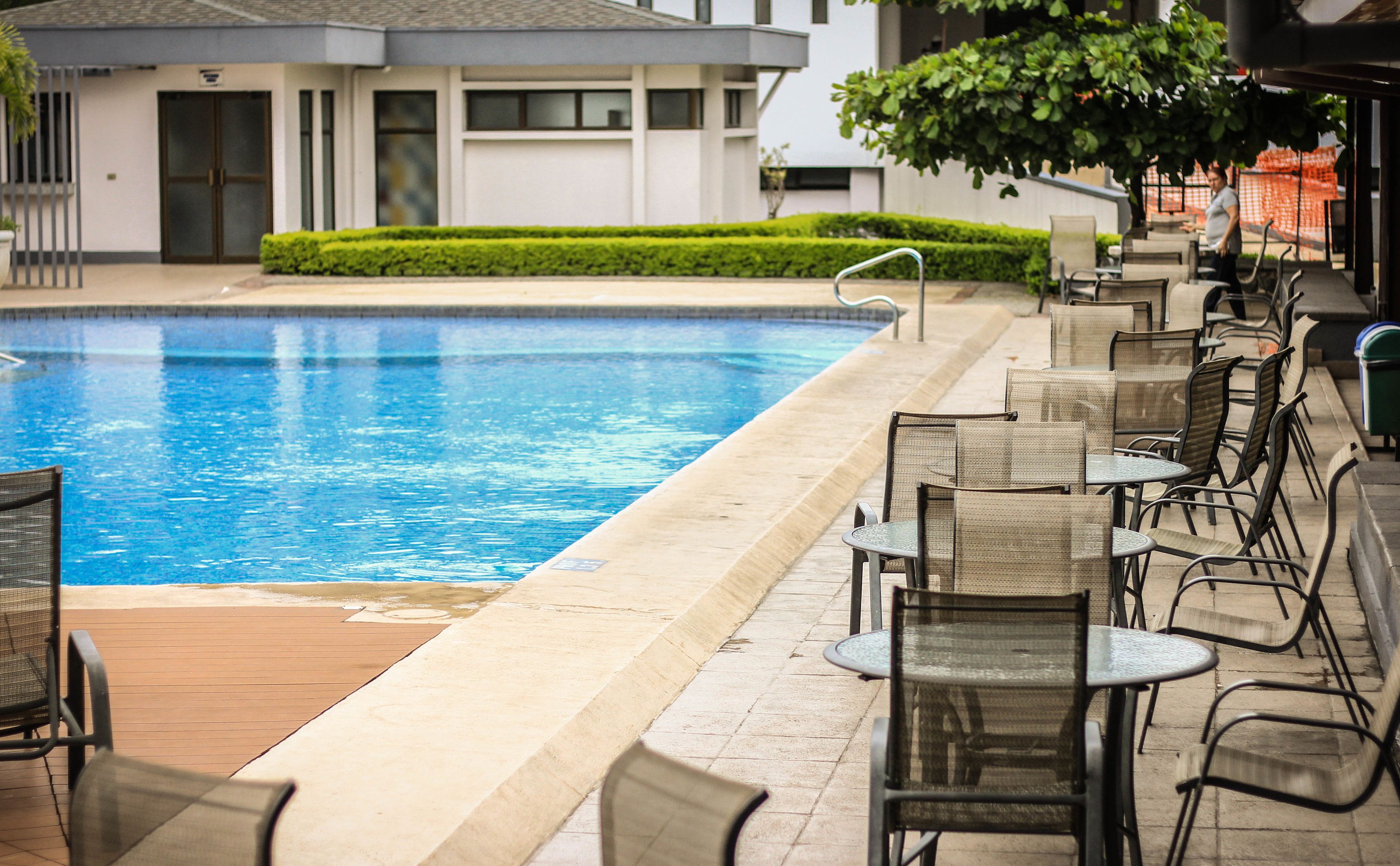 Piscina con bordo in legno e area relax esterna con sedie e tavoli.