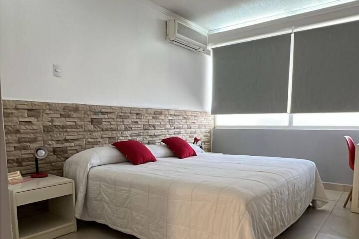 A bedroom with a bed, a nightstand, a red chair, and a window.