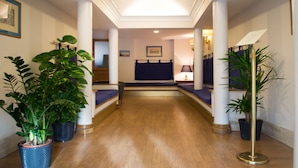 Un hall de hotel con piso de madera, asientos azules y plantas en macetas.