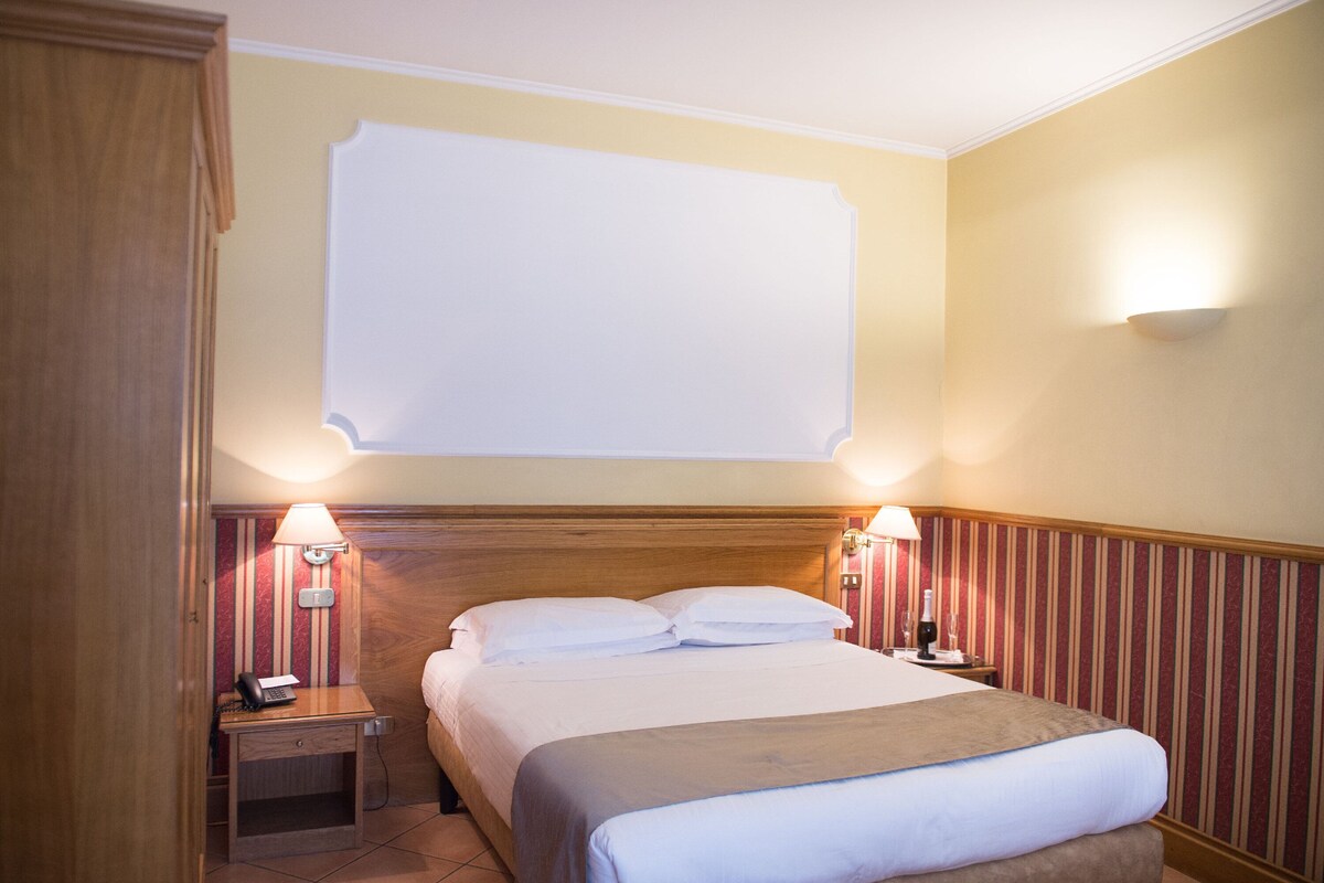 A hotel room with a bed, bedside lamps, a nightstand, and a wall-mounted TV.