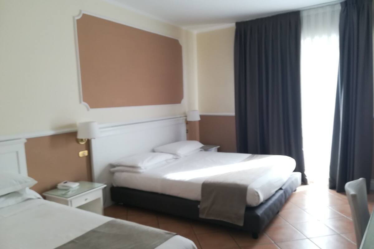 A hotel room with a bed, bedside table, lamp, and curtains.