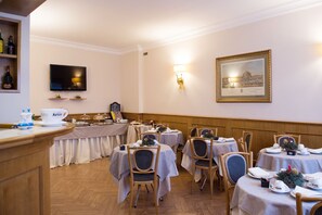 A dining area with multiple tables and chairs, a television mounted on the wall, and a framed picture above the tables. - Hotel Leopardi (Naples)