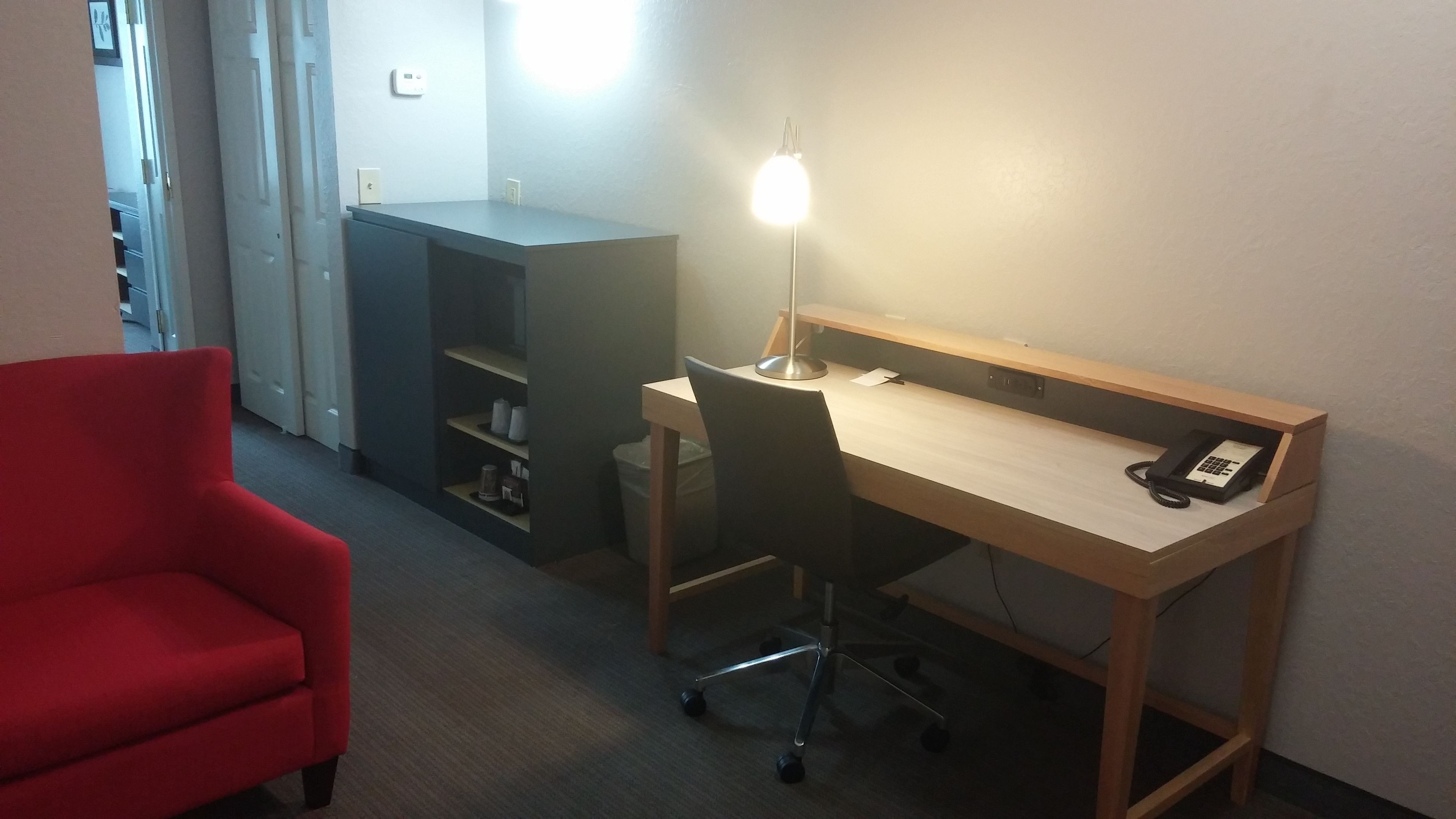 A hotel room with a wooden desk, a red armchair, a desk lamp, and a telephone.