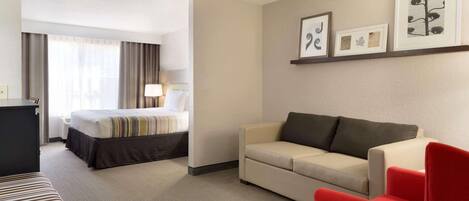 Une chambre d’hôtel avec un lit, un canapé, un fauteuil rouge, un bureau et une lampe. Des tableaux encadrés ornent le mur.