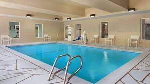 An indoor swimming pool with clear blue water, surrounded by white chairs and a tiled floor.