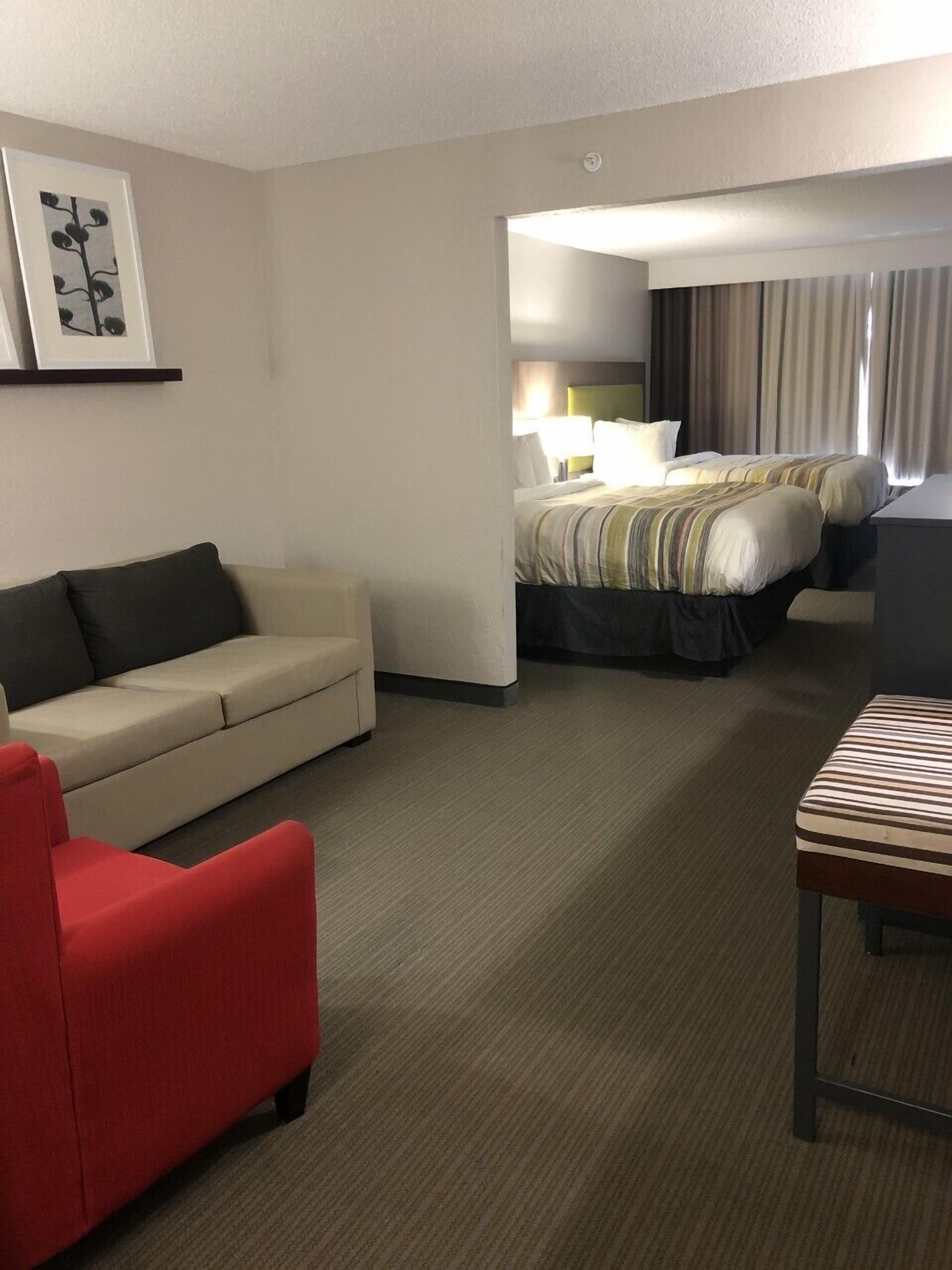 A hotel room with a sofa, a red chair, a bed with striped bedding, and a small table.