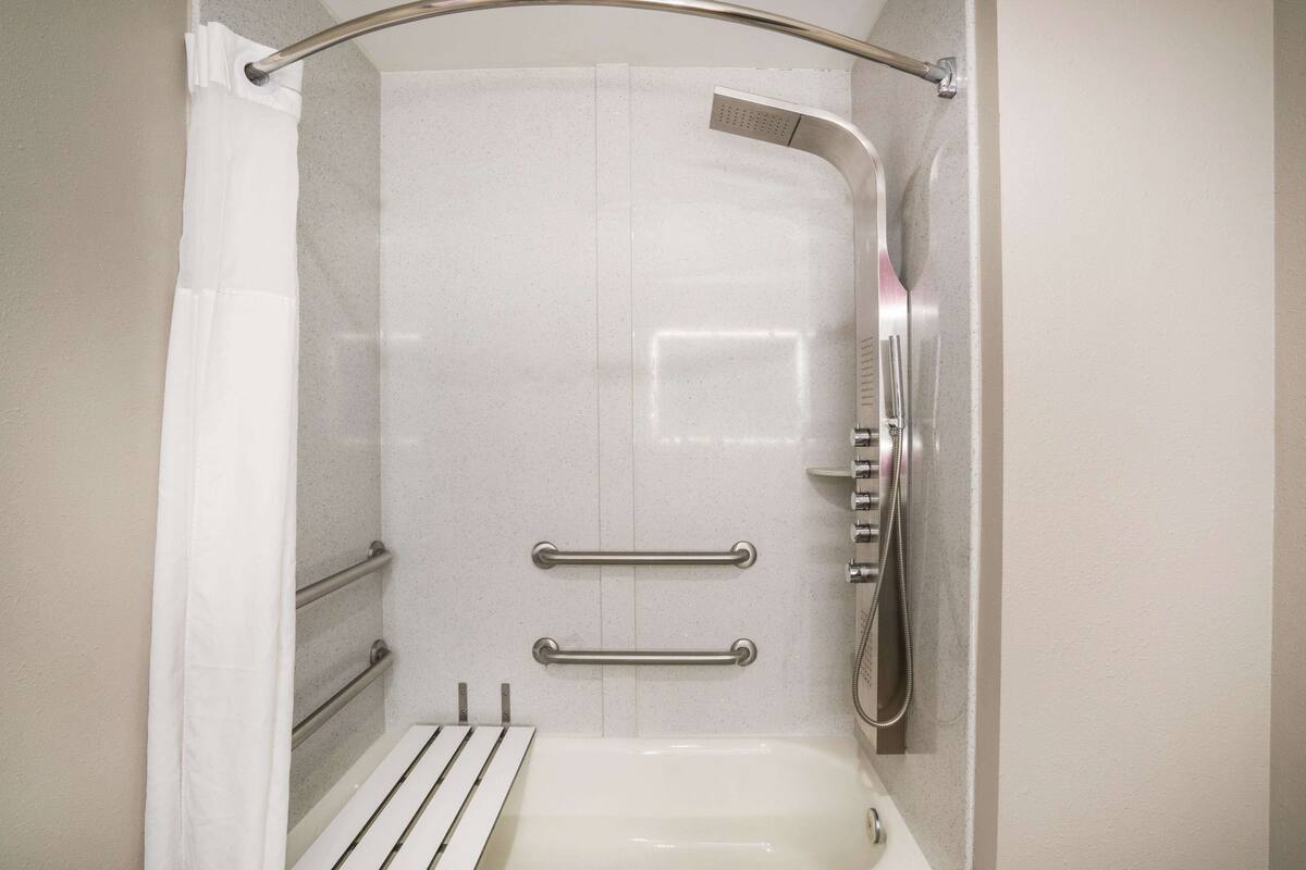 Ein modernes Duschbad mit Handbrause, Haltegriffen und einer weißen Badewanne.