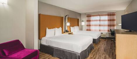 A hotel room with two beds, a desk, a TV, a red sofa, and a wooden floor.