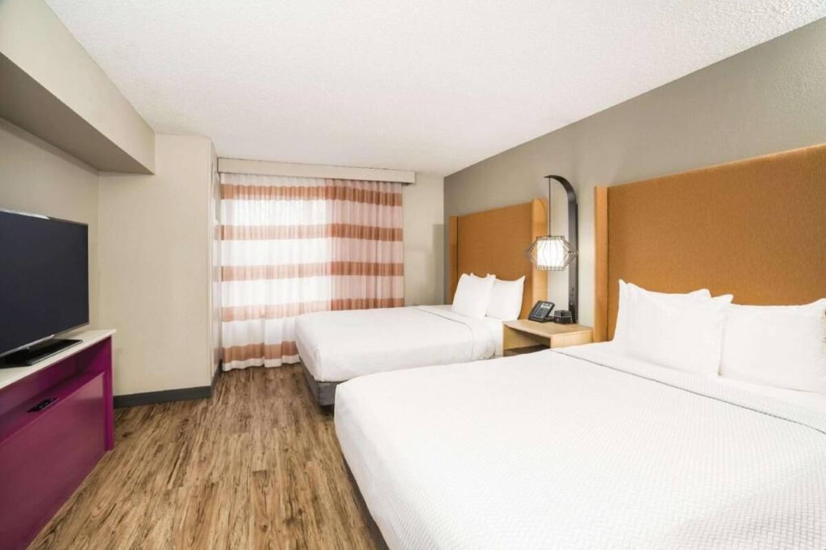 Ein Hotelzimmer mit zwei Betten, einem Fernseher, einem Schreibtisch und einem Fenster mit Vorhängen.