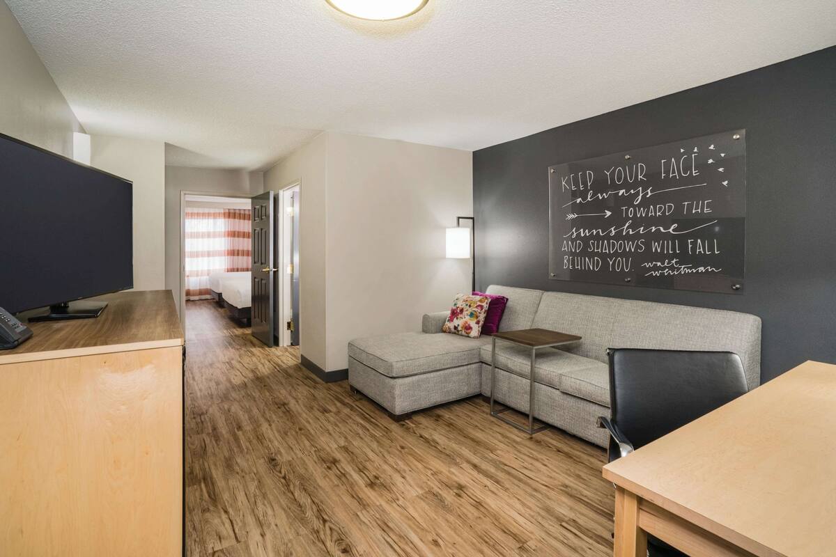 Ein modernes Zimmer mit einem Holztisch, einem grauen Sofa und einem motivierenden Zitat an der Wand.
