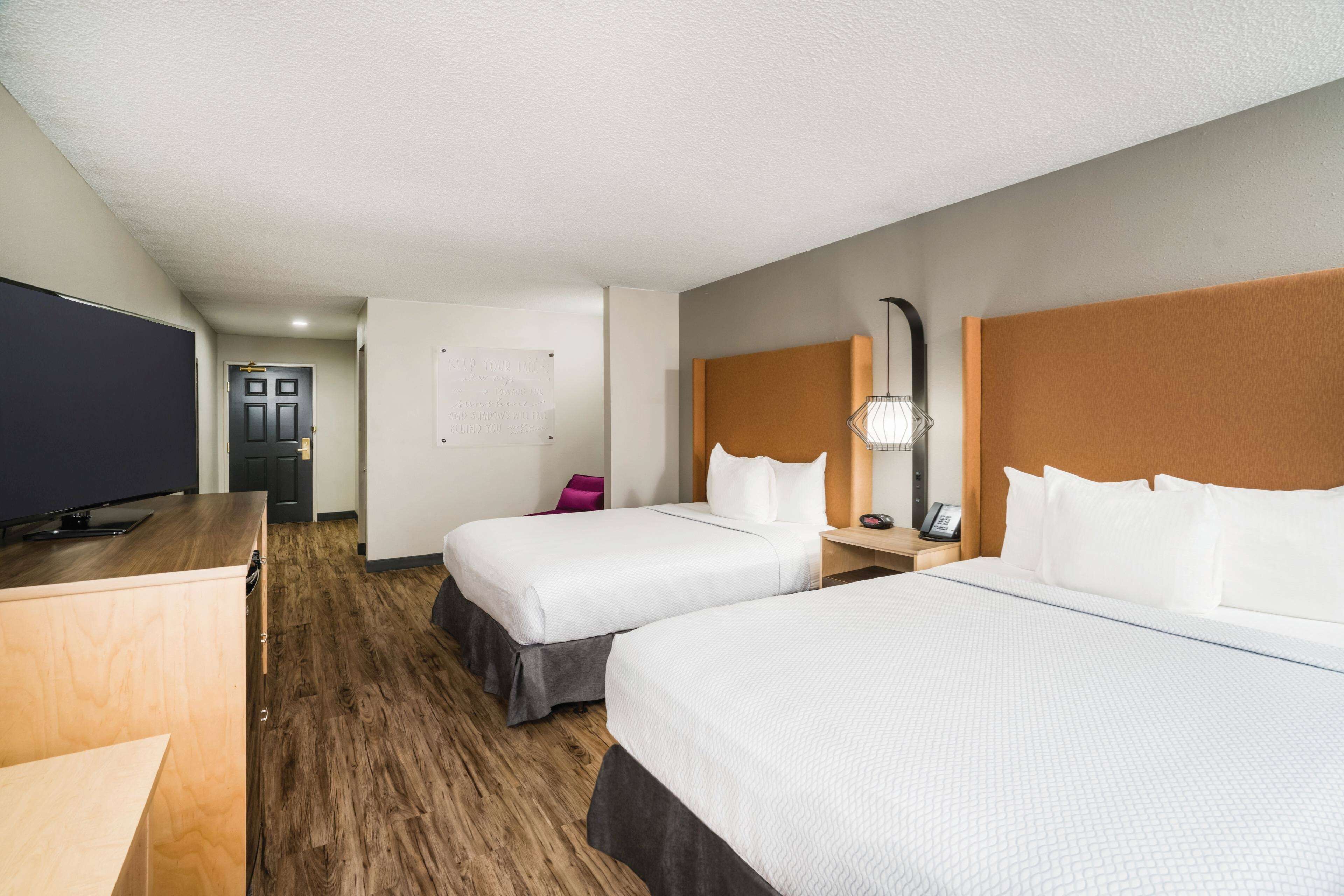 A hotel room with two beds, a desk, a television, and a door.