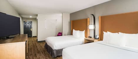 A hotel room with two beds, a desk, a television, and a door.