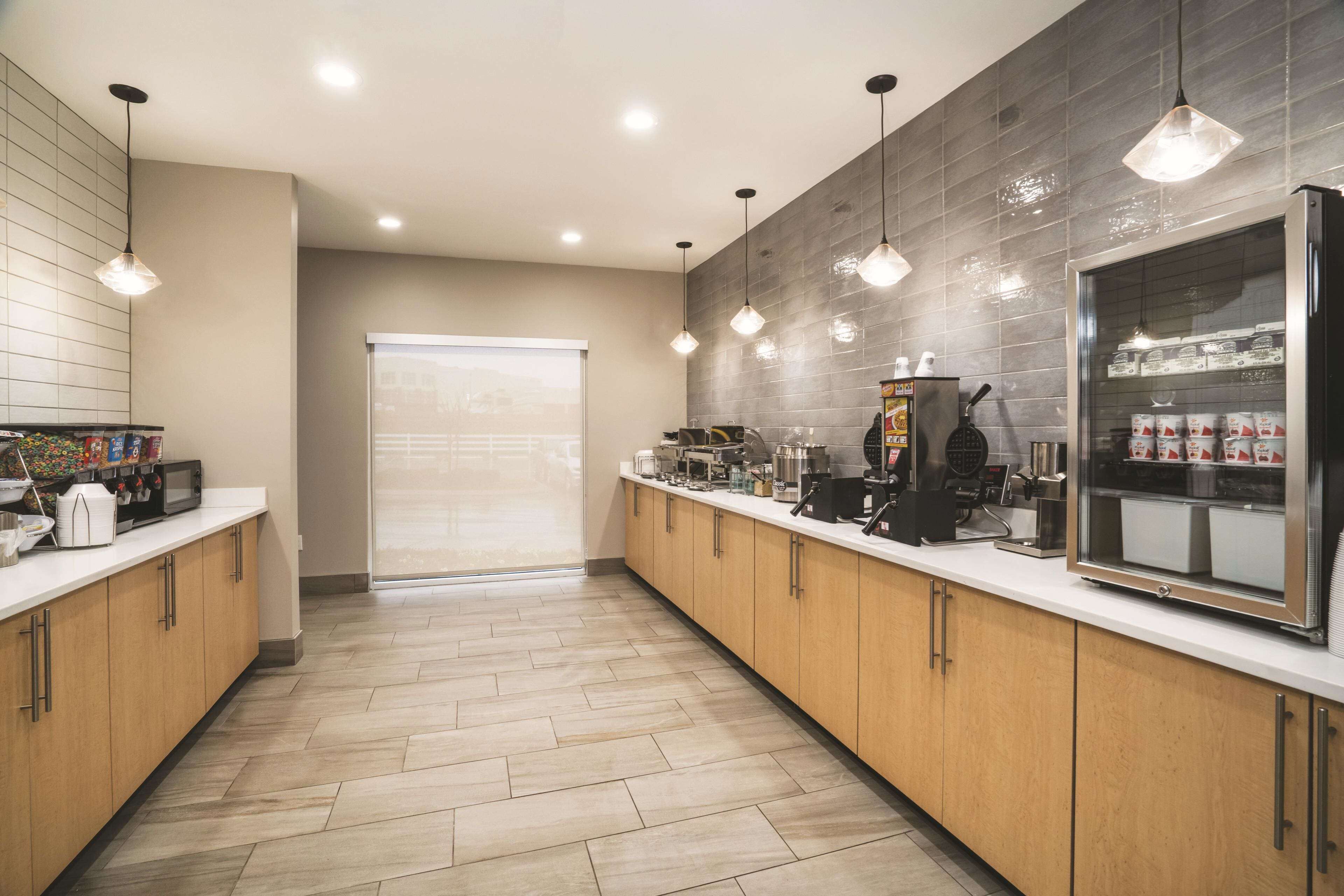 A modern kitchen with wooden cabinets, a stainless steel refrigerator, and a coffee station.
