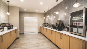 A modern kitchen with wooden cabinets, a stainless steel refrigerator, and a coffee station.