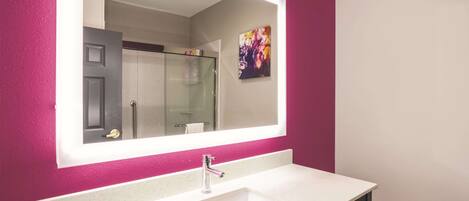 Une salle de bain avec un lavabo blanc, un grand miroir et une douche en verre.