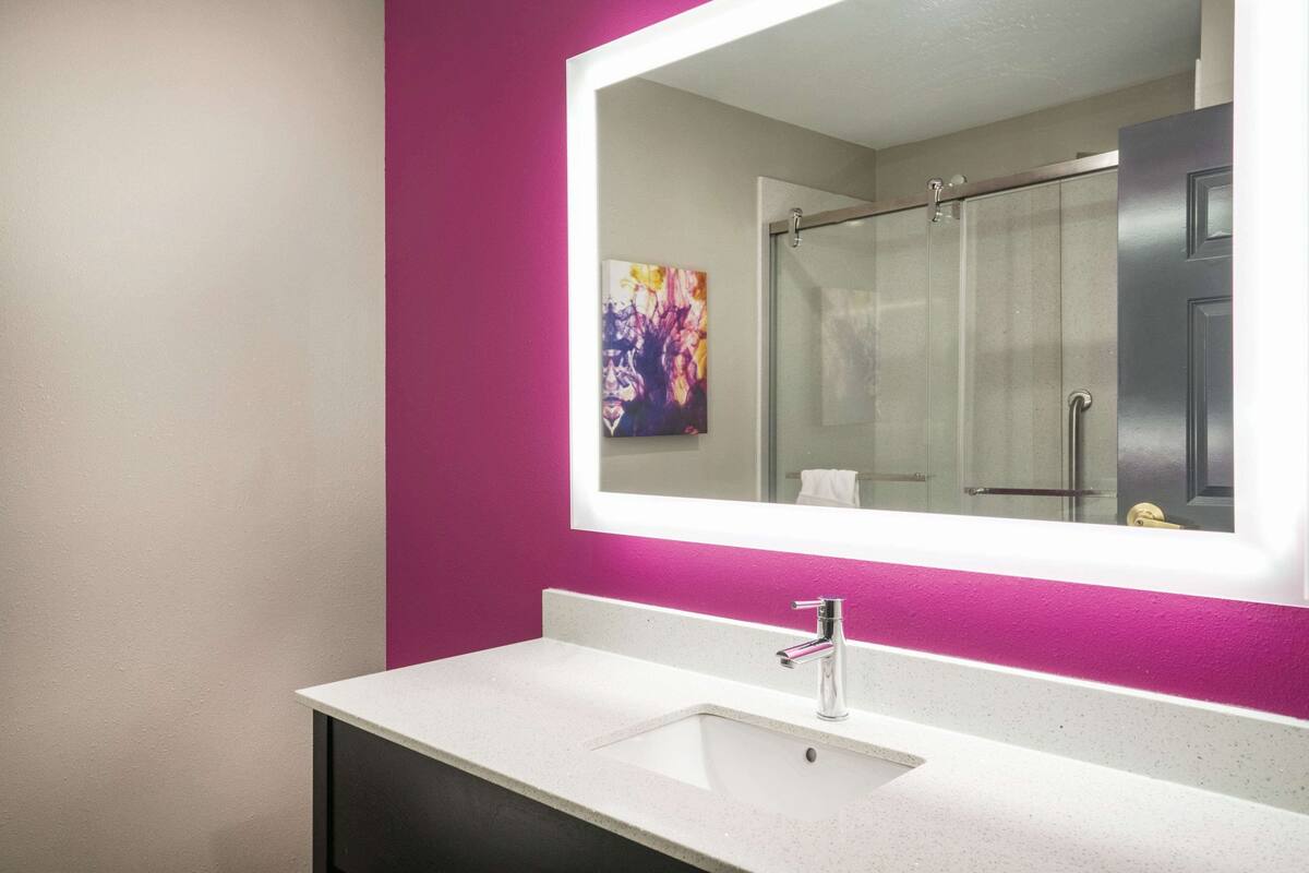 Ein modernes Badezimmer mit einem weißen Waschbecken, einem großen Spiegel und einer Dusche.