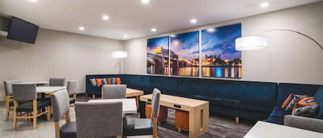 A modern lounge area with a dining table, chairs, a sofa, and a large cityscape painting on the wall.