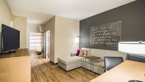 Un salon moderne avec un canapé d’angle, un téléviseur à écran plat, un bureau en bois et un mur recouvert d’un tableau noir sur lequel sont écrits des messages motivants.