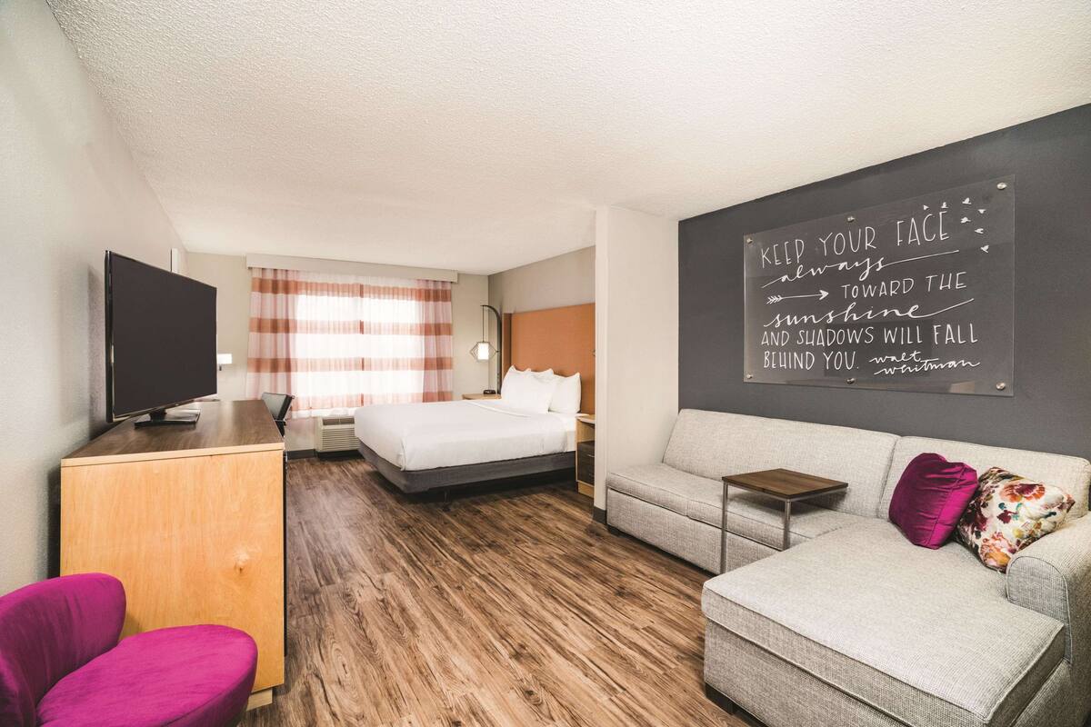 Ein Hotelzimmer mit Bett, einer Couch, einem Fernseher und einer Tafel mit einem Motivationsspruch.