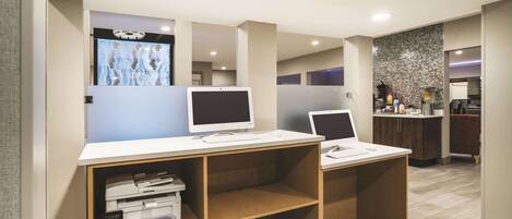 A modern office space with two desks, each with a computer and keyboard, and a printer on the left.