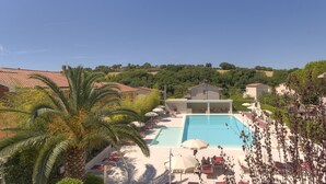 Zona de piscina con tumbonas y sombrillas, rodeada de edificios y vegetación.