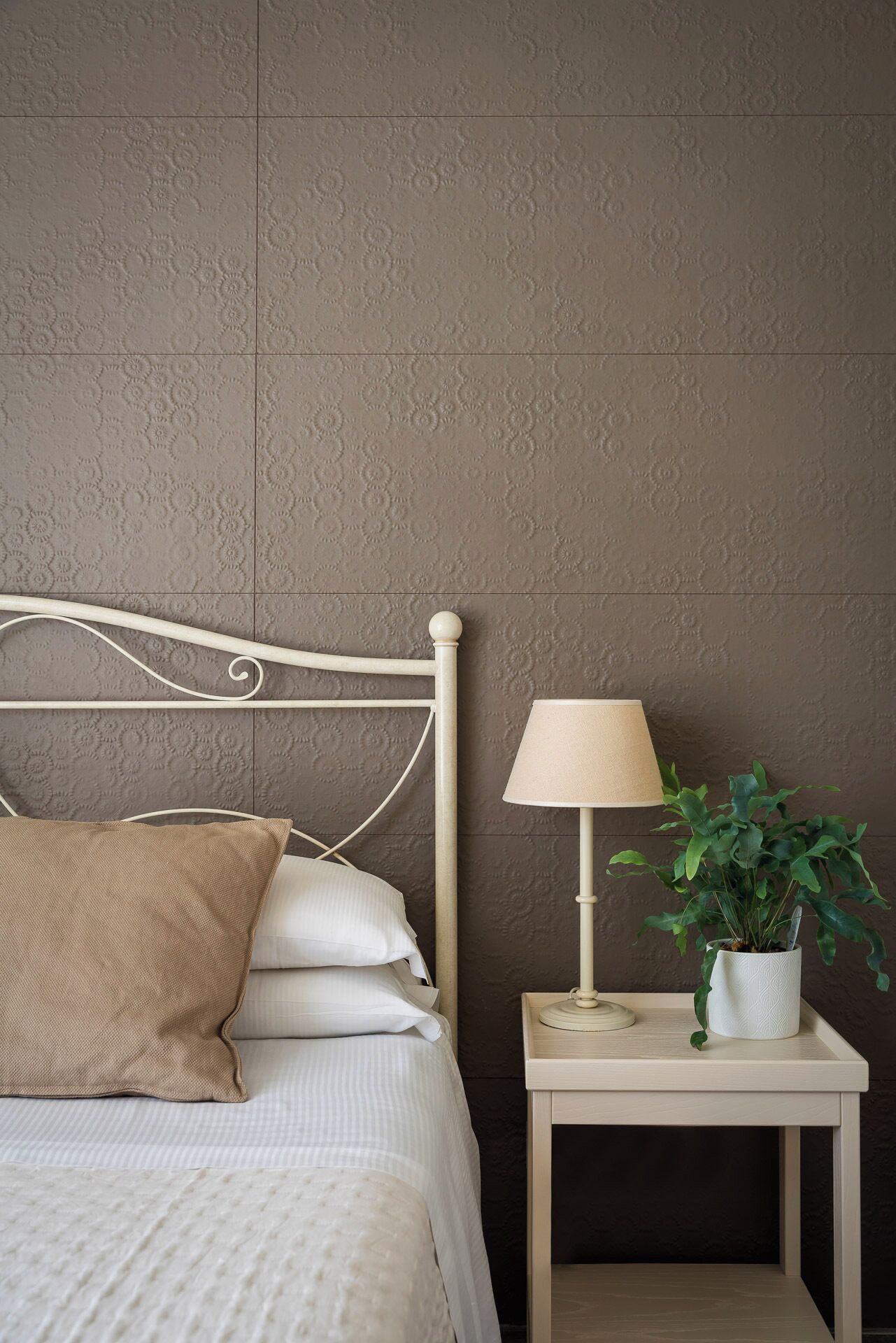 A neatly made bed with a headboard, a bedside lamp, and a small table with a plant.