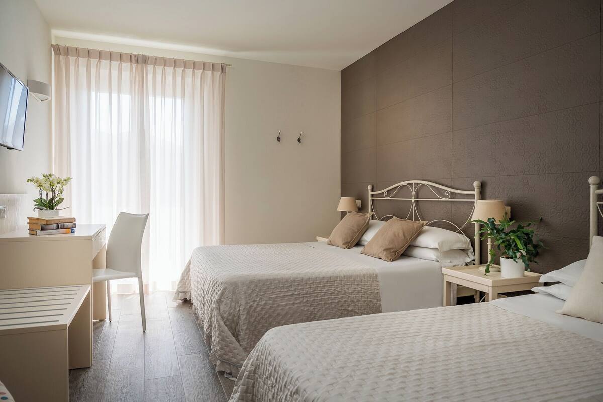 A hotel room with two beds, a desk, a chair, a TV, and a window with curtains.