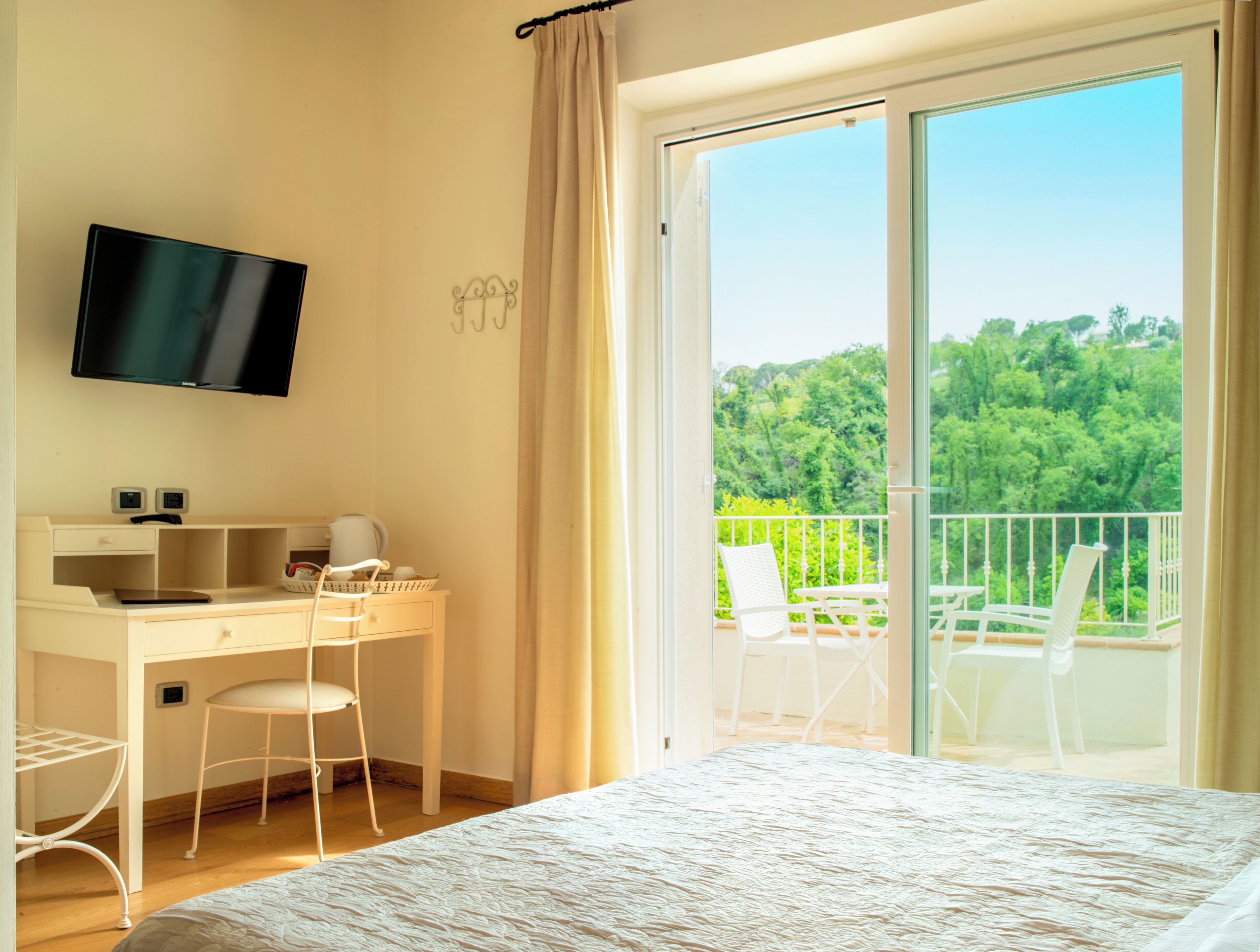 Un dormitorio con cama, escritorio, silla, televisor y balcón con vistas a zonas verdes.