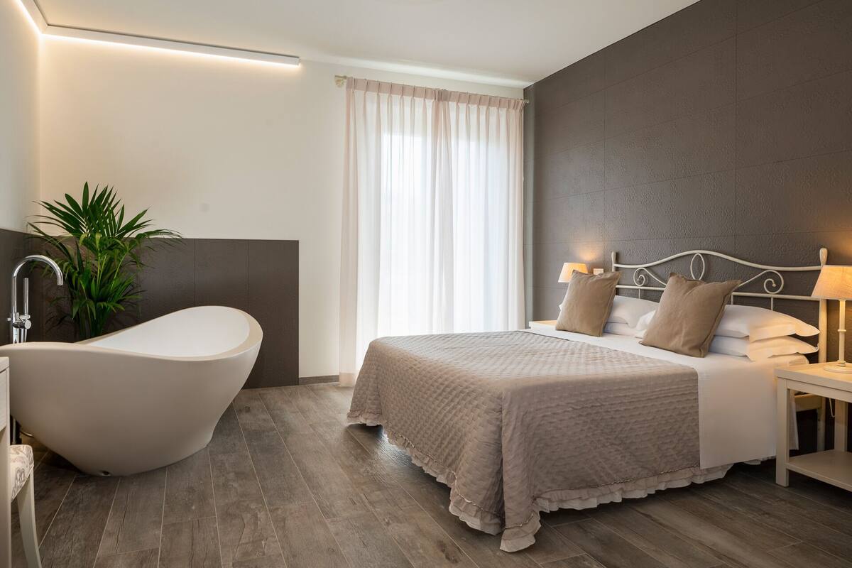 A modern bedroom with a large bed, a bathtub, and a nightstand with a lamp.