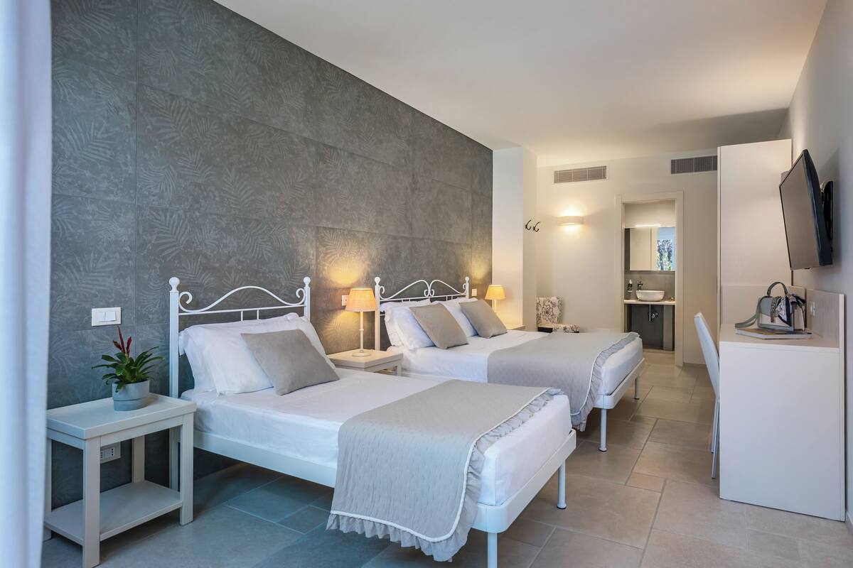 A hotel room with two beds, a small table with a plant, a desk with a chair, and a TV on the wall.