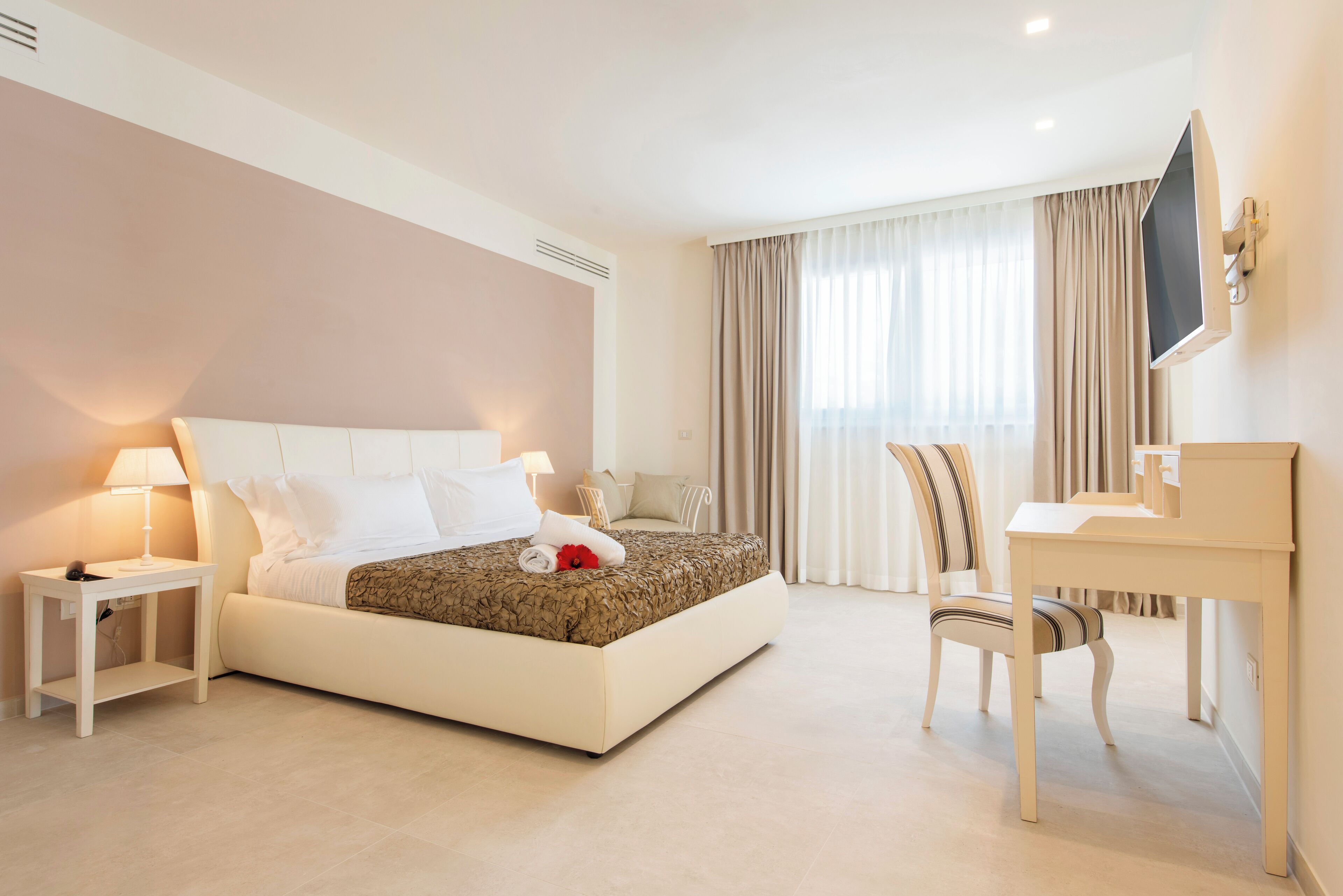 A modern hotel room with a large bed, bedside tables, a desk, and a TV.
