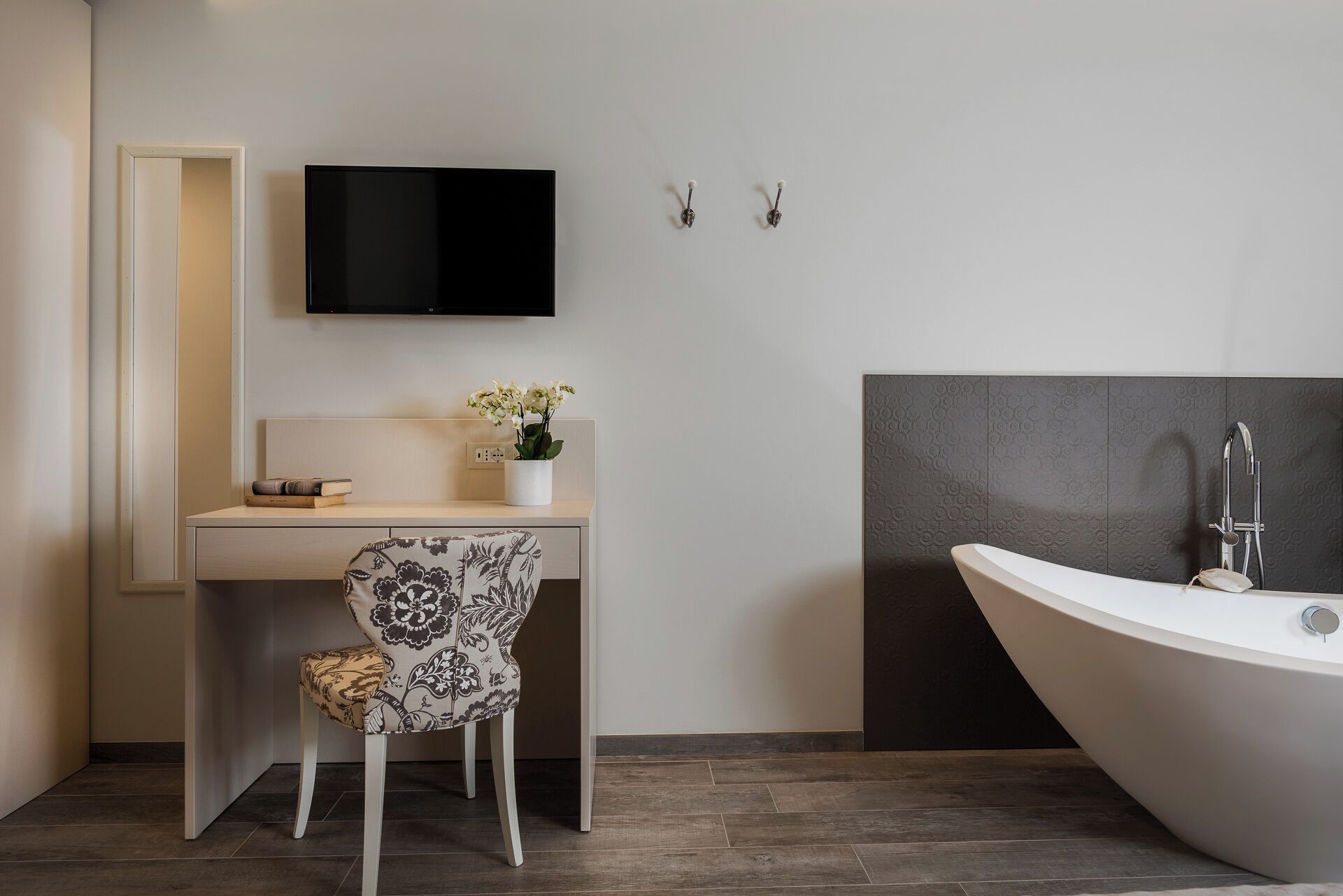 A modern bathroom with a freestanding bathtub, a small desk with a chair, and a mounted TV.
