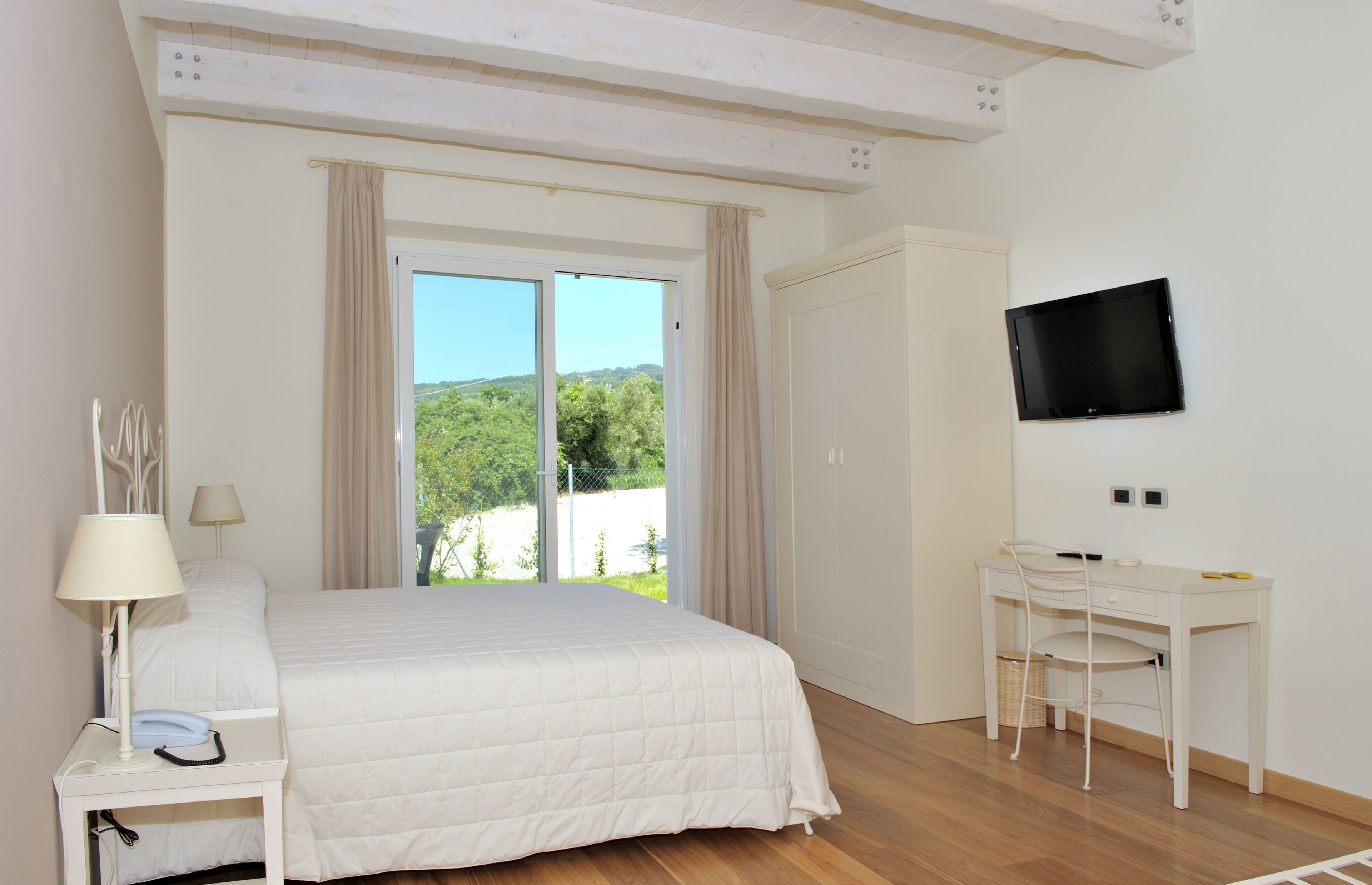 A bedroom with a bed, a desk, a chair, a TV, and a window with curtains.