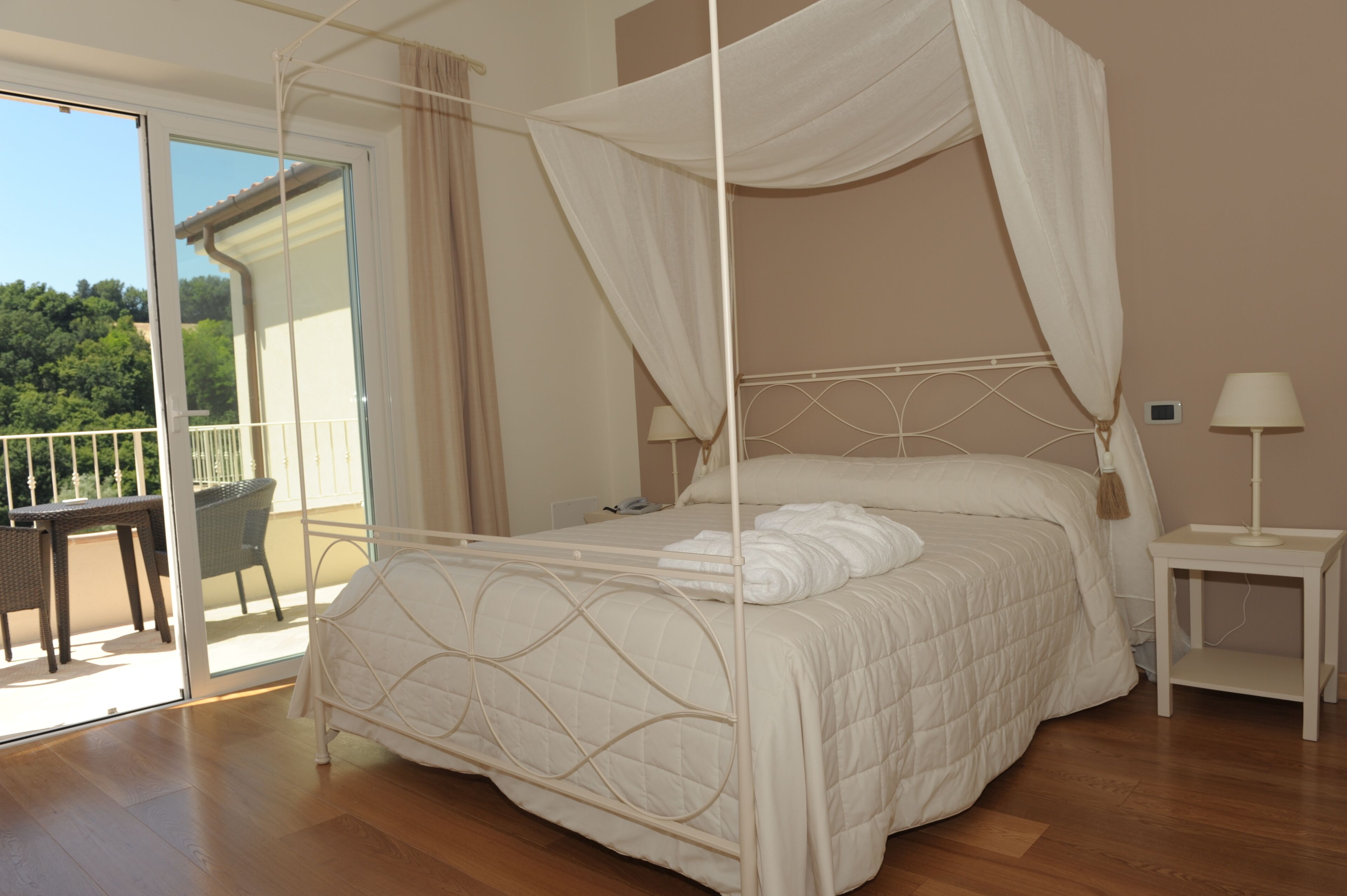 Una camera da letto con un letto a baldacchino, un comodino con una lampada e vista su un balcone con mobili da esterno.