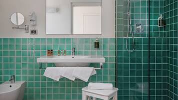 Un baño con un lavabo blanco, un espejo, un perchero para toallas, un cabezal de ducha de mano y paredes con azulejos verdes.