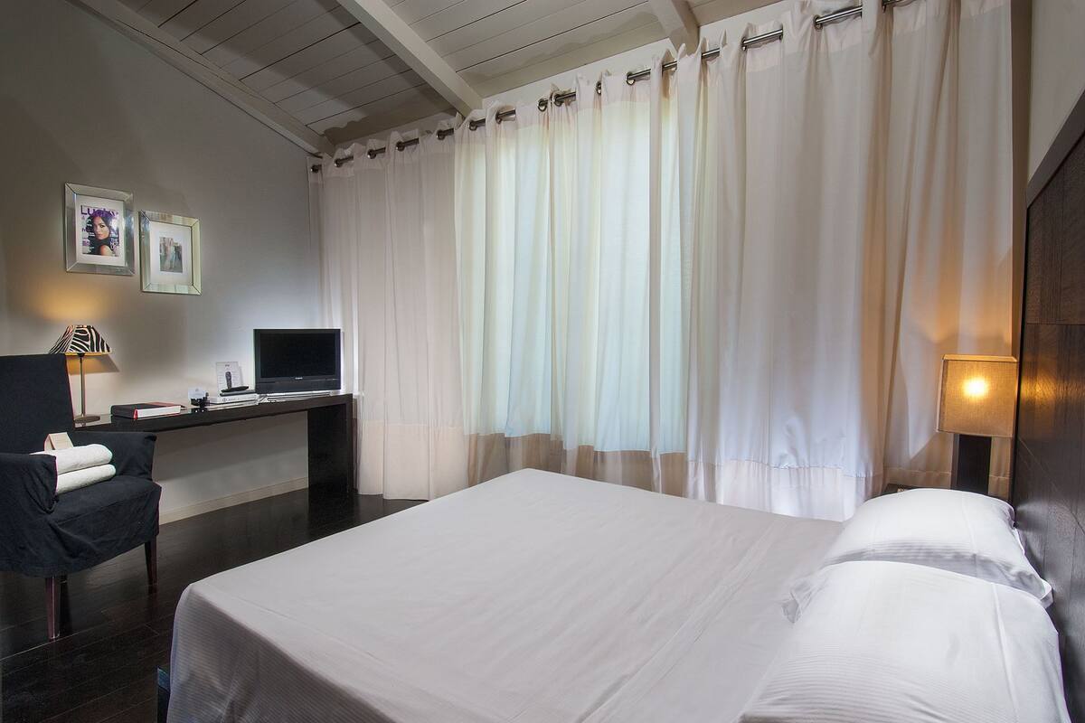 A hotel room with a bed, a desk with a computer, a chair, and curtains.