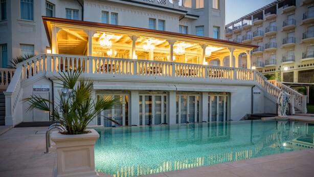 A hotel with a pool, a covered area with a railing, and a staircase leading to an upper level. - Hotel Carducci 76 (Cattolica)