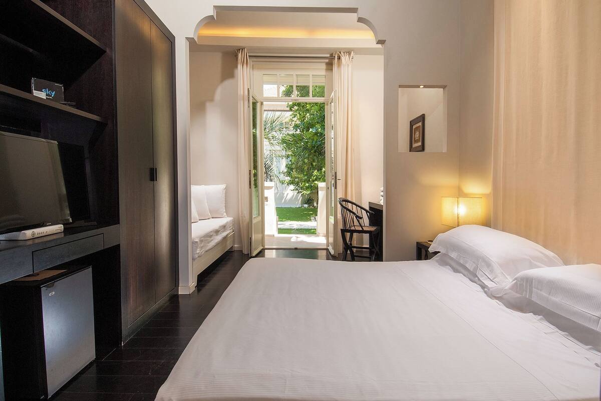A hotel room with a bed, a desk, a chair, a TV, and a view of the outdoors.
