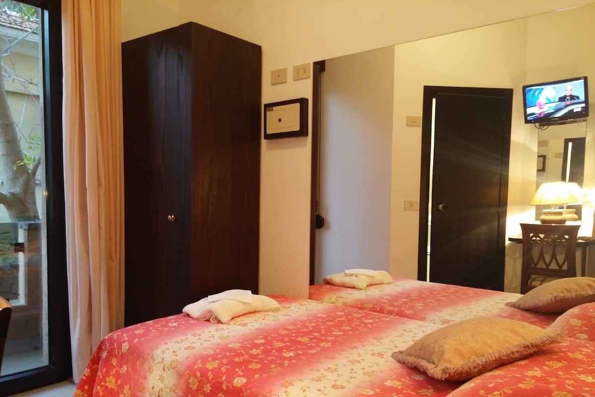 A hotel room with a large bed, a wardrobe, a television, and a desk with a lamp.