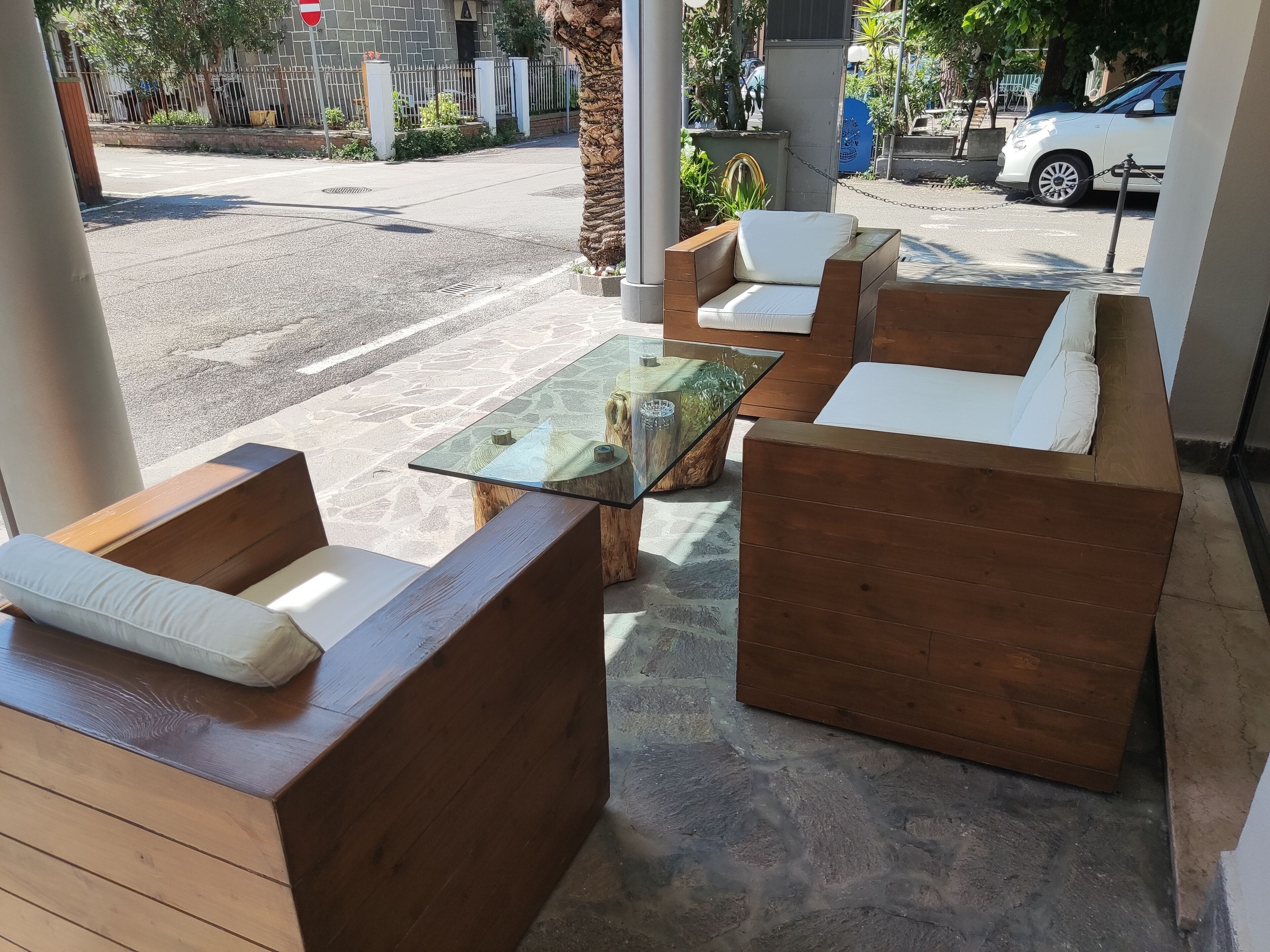 A seating area with wooden furniture and a glass-top table, set on a stone floor with a view of the street.