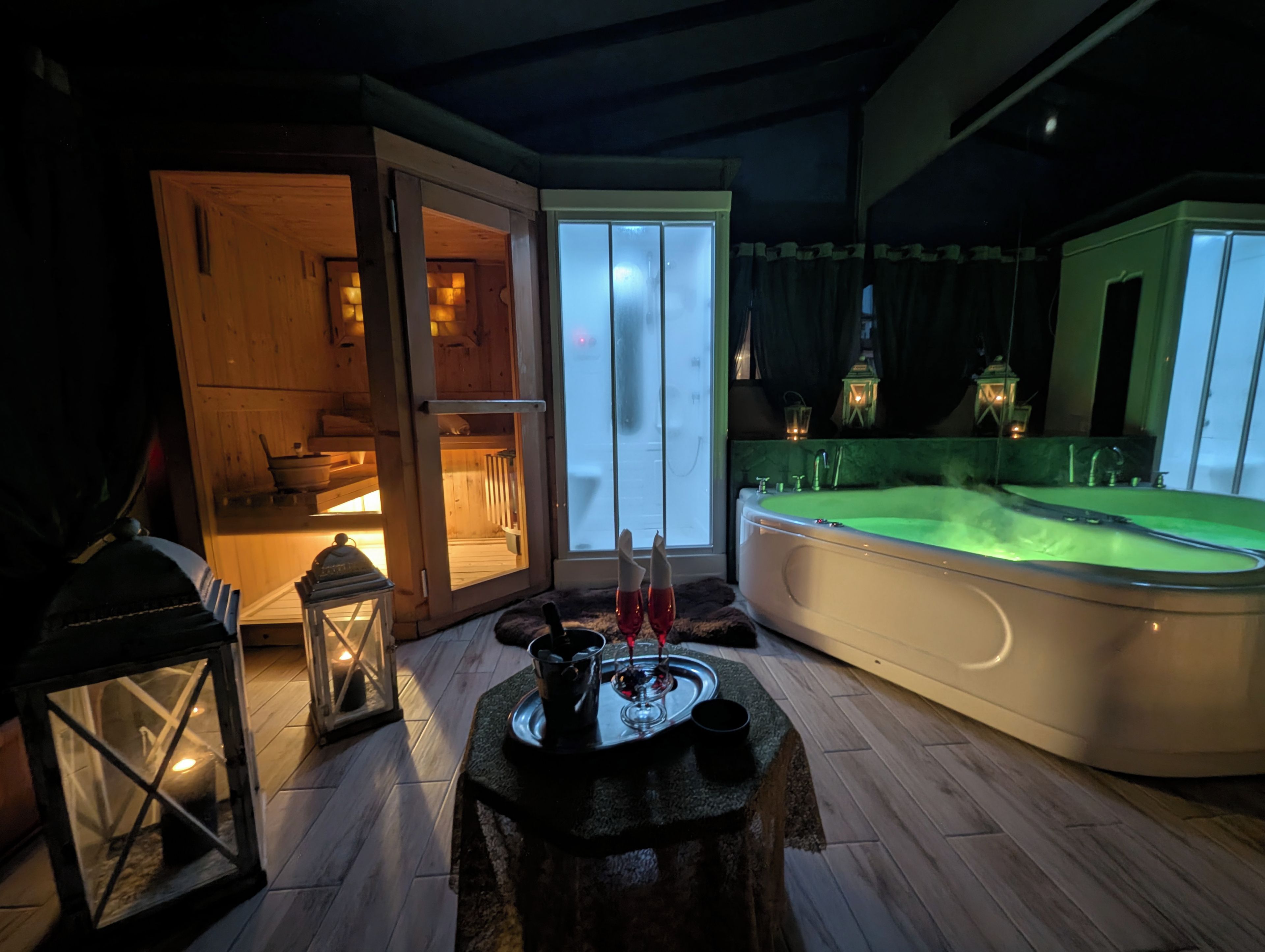 Una habitación con una bañera grande, una puerta de madera que da a un balcón y una mesa con una vela y un vaso.