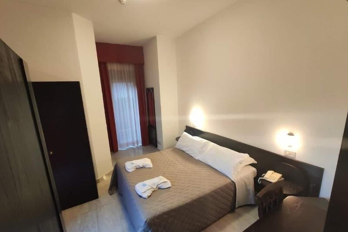 A hotel room with a bed, bedside table, and a desk with a chair.