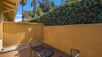 A patio with two metal chairs and a small round table, a wooden fence, and a hedge.