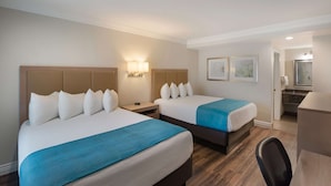 Habitación de hotel con dos camas, un escritorio y un baño visible a través de una puerta abierta.