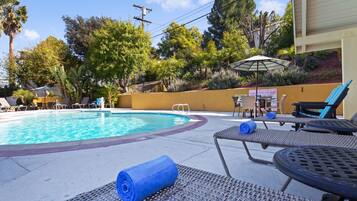A pool area with lounge chairs and a table, surrounded by trees and a yellow wall.